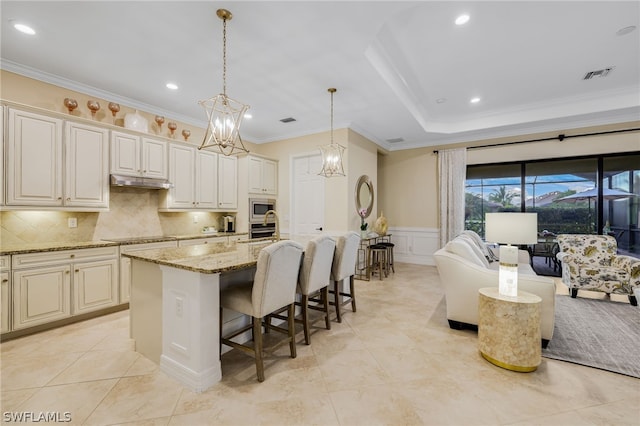 kitchen with a breakfast bar, a center island with sink, decorative light fixtures, light stone counters, and stainless steel appliances