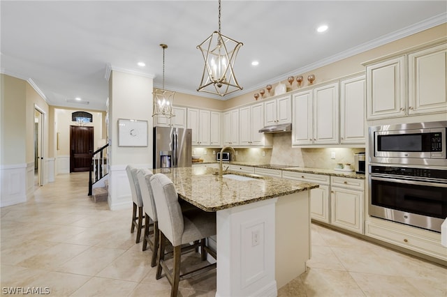 kitchen with pendant lighting, sink, an island with sink, light stone counters, and stainless steel appliances