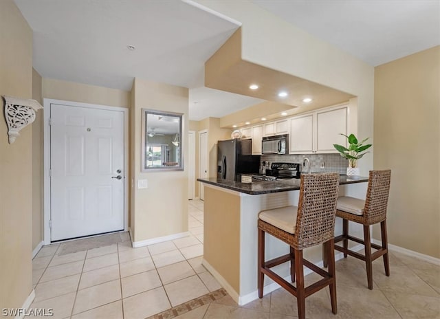 kitchen with a breakfast bar, range, backsplash, white cabinetry, and kitchen peninsula