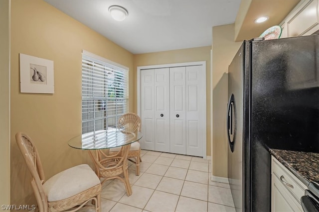 kitchen featuring stove, black fridge, light tile flooring, white cabinetry, and dark stone counters