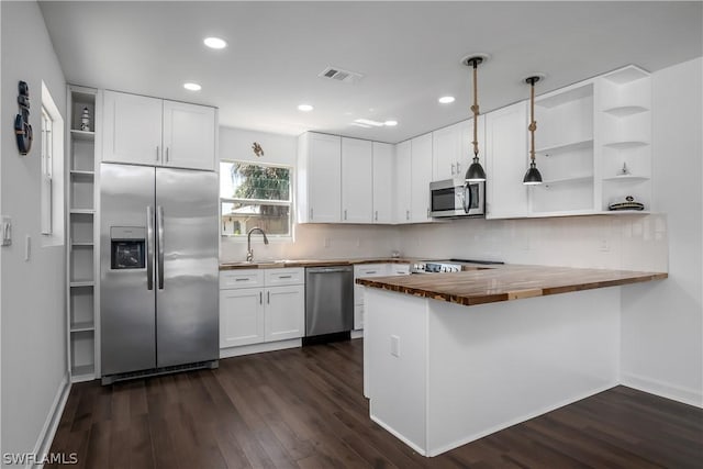 kitchen featuring kitchen peninsula, appliances with stainless steel finishes, butcher block countertops, white cabinetry, and hanging light fixtures