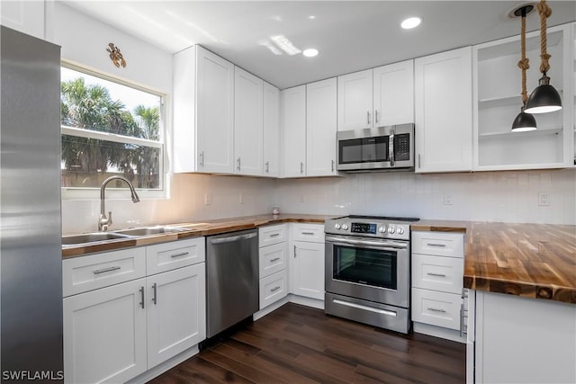 kitchen with wooden counters, white cabinets, sink, decorative light fixtures, and stainless steel appliances