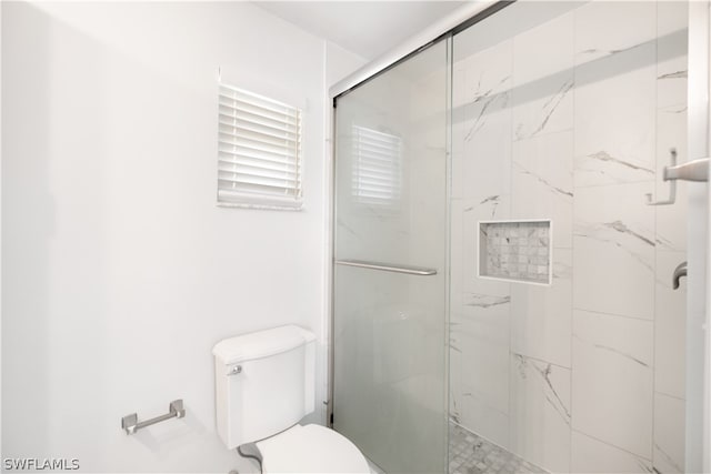 bathroom featuring a shower with door and toilet