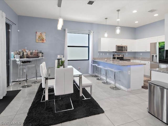 interior space featuring hanging light fixtures, appliances with stainless steel finishes, a kitchen breakfast bar, and white cabinetry