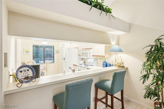 kitchen featuring white cabinets, a breakfast bar, white appliances, and kitchen peninsula