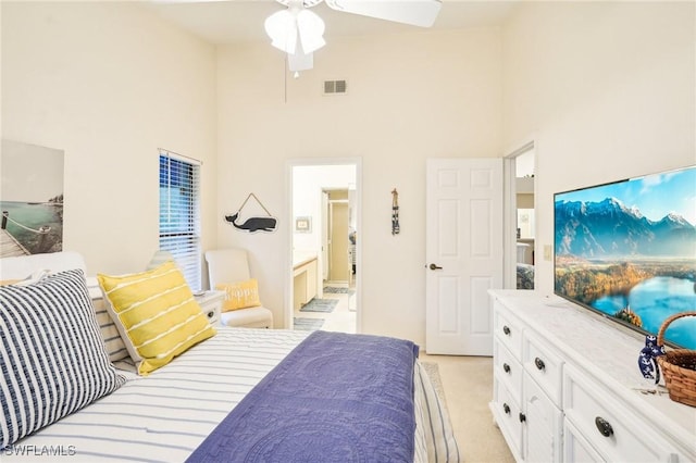 bedroom featuring ceiling fan, ensuite bathroom, a towering ceiling, and light carpet