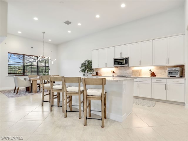 kitchen featuring backsplash, a notable chandelier, a center island with sink, and white cabinetry