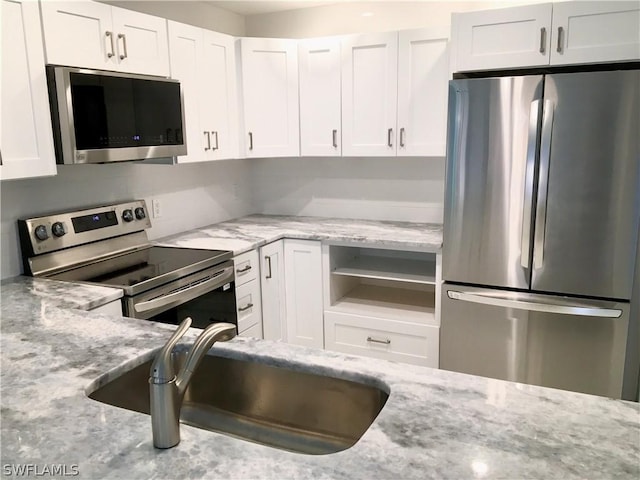 kitchen featuring light stone counters, stainless steel appliances, white cabinetry, and sink