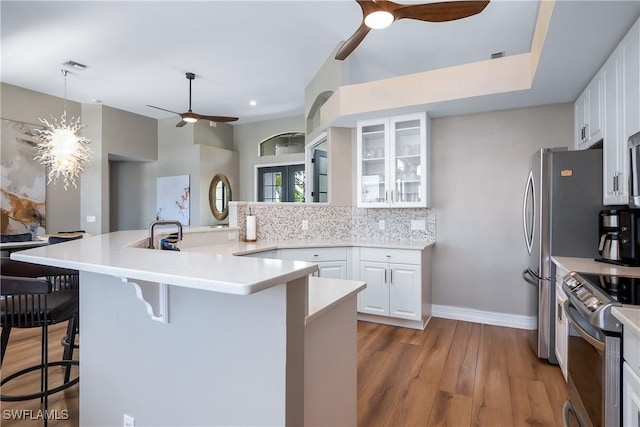 kitchen with a breakfast bar area, light countertops, glass insert cabinets, appliances with stainless steel finishes, and white cabinetry