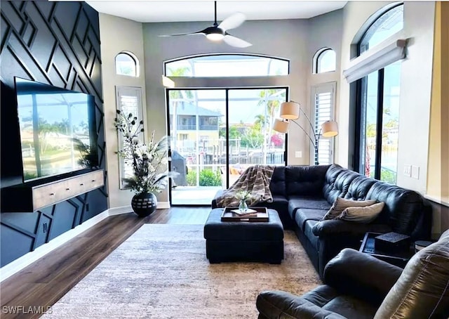 living area featuring a healthy amount of sunlight, a ceiling fan, baseboards, and dark wood-type flooring