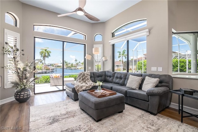 living area featuring a water view, a sunroom, ceiling fan, wood finished floors, and baseboards