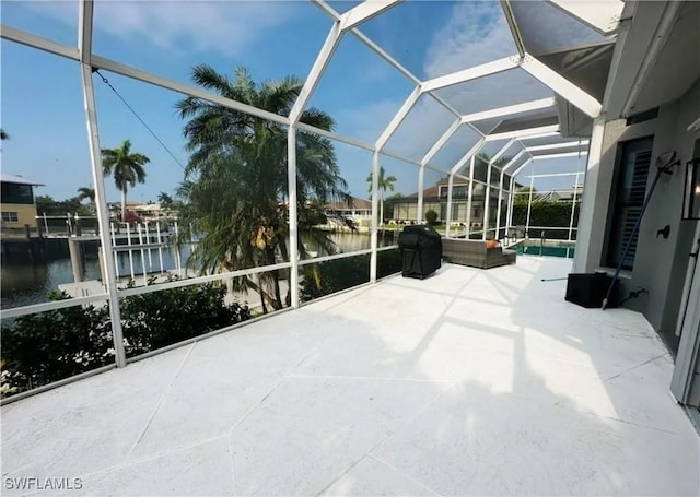 view of patio with a water view, glass enclosure, and area for grilling