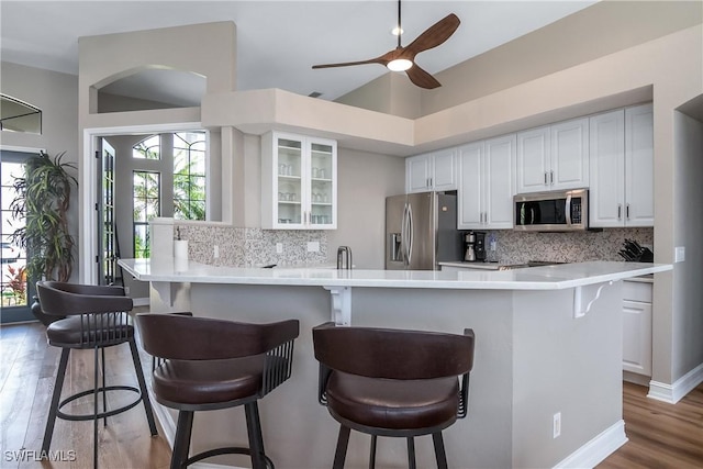 kitchen with white cabinets, glass insert cabinets, a breakfast bar, appliances with stainless steel finishes, and light countertops