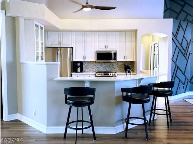 kitchen featuring tasteful backsplash, a breakfast bar area, glass insert cabinets, stainless steel appliances, and light countertops