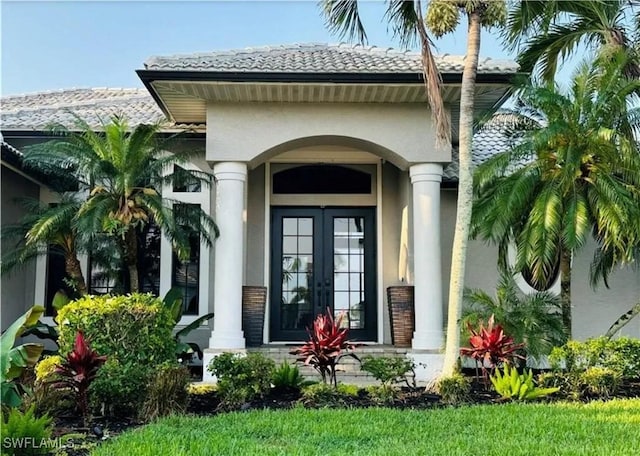 view of exterior entry featuring a tiled roof, french doors, and stucco siding