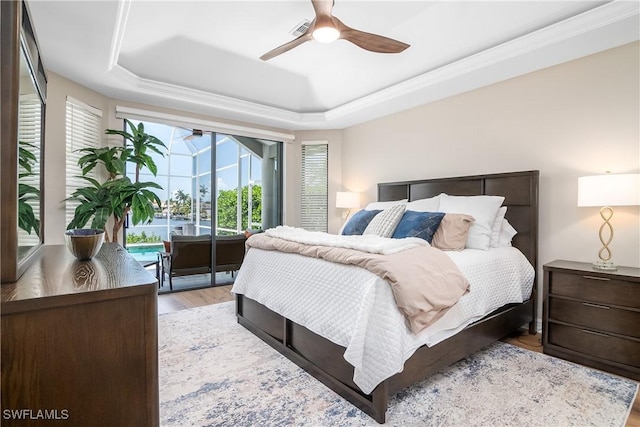 bedroom featuring a tray ceiling, access to outside, a ceiling fan, a sunroom, and light wood-type flooring