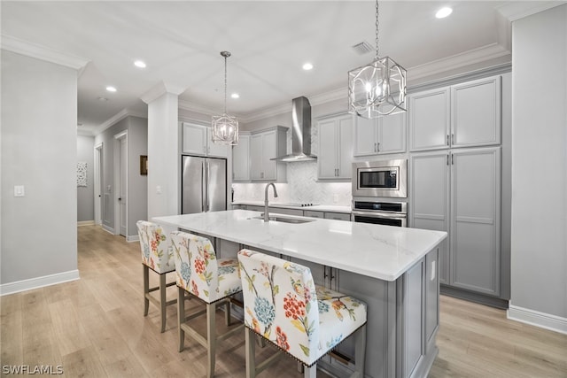 kitchen with decorative light fixtures, wall chimney range hood, light wood-type flooring, and stainless steel appliances