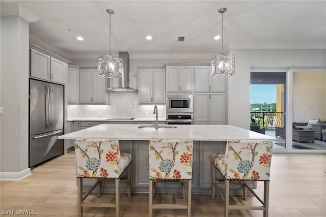 kitchen featuring decorative light fixtures, light hardwood / wood-style flooring, stainless steel appliances, wall chimney range hood, and sink