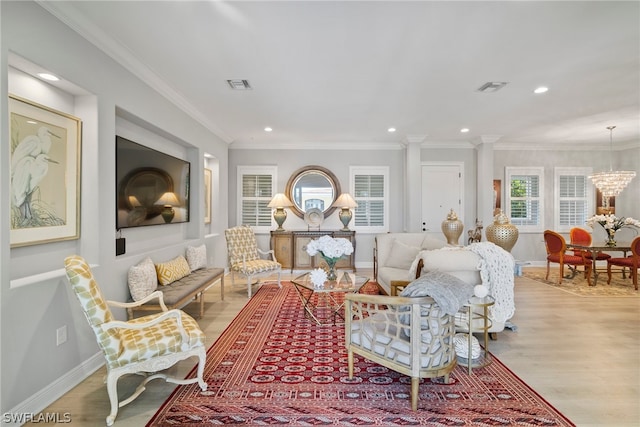 living room featuring ornate columns, crown molding, light wood-type flooring, and a chandelier