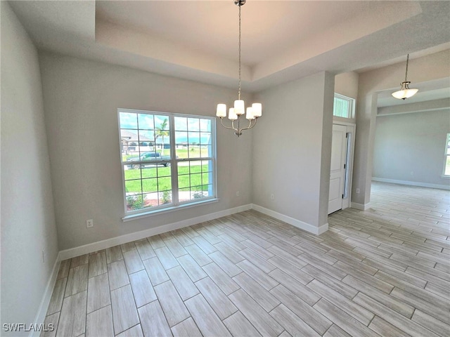 unfurnished room with light hardwood / wood-style flooring, a tray ceiling, and an inviting chandelier