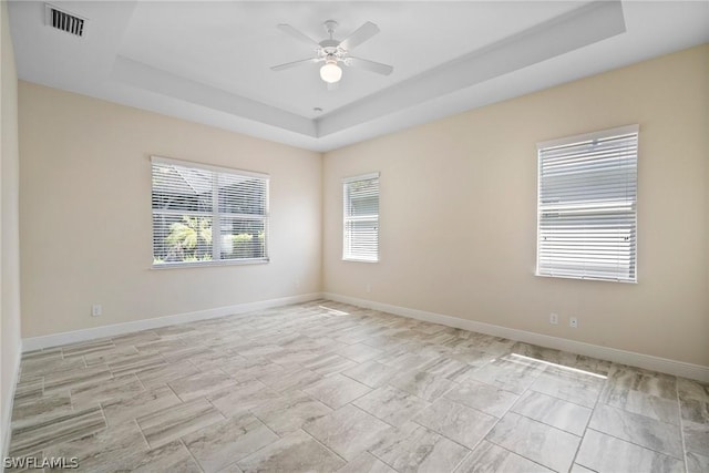 unfurnished room featuring visible vents, a tray ceiling, ceiling fan, and baseboards