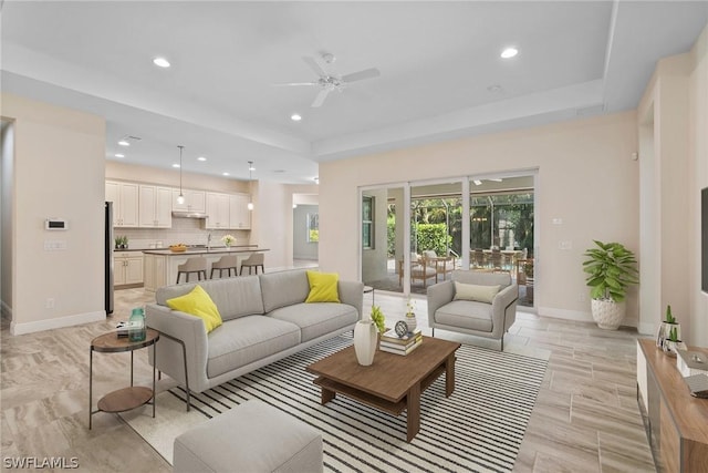 living room featuring recessed lighting, a raised ceiling, ceiling fan, and baseboards