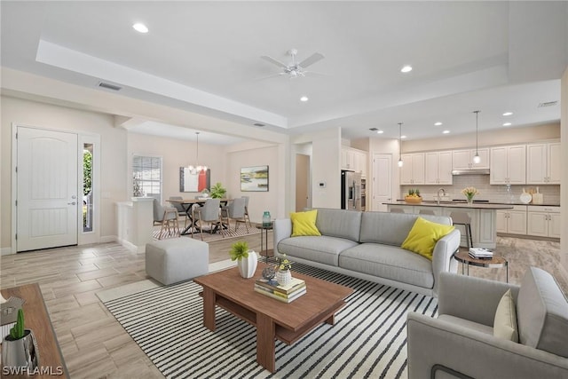 living room featuring a tray ceiling, recessed lighting, visible vents, a ceiling fan, and baseboards