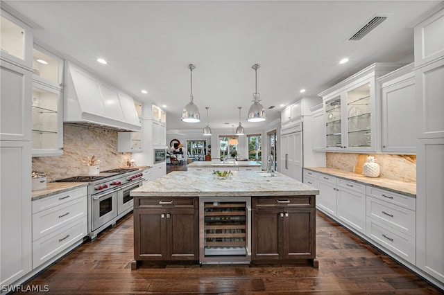 kitchen with custom range hood, premium appliances, beverage cooler, pendant lighting, and white cabinetry