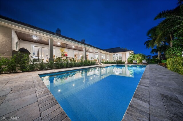 pool at night featuring a patio area