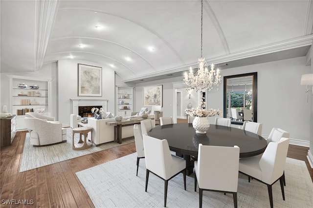 dining room with built in features, wood-type flooring, ornamental molding, and an inviting chandelier