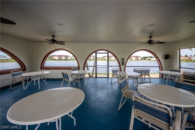 dining room featuring finished concrete flooring, a water view, and ceiling fan