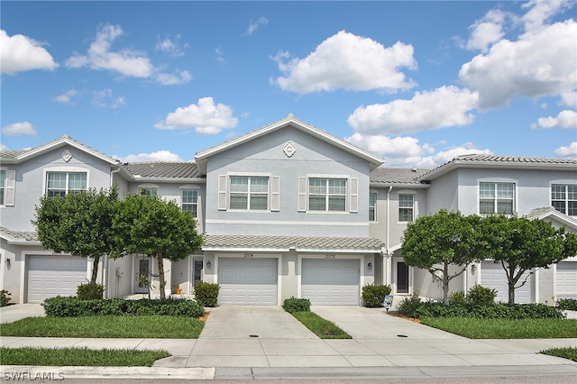 townhome / multi-family property featuring an attached garage, driveway, a tiled roof, and stucco siding