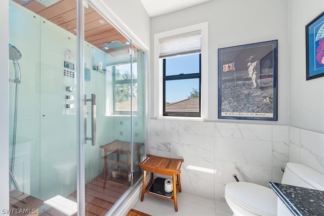 bathroom featuring a shower with shower door, tile floors, tile walls, vanity, and toilet