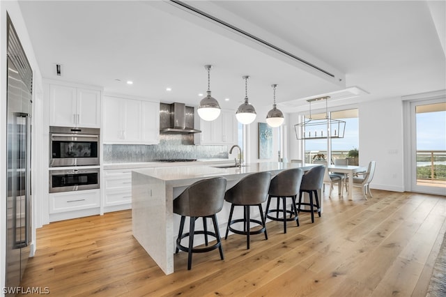 kitchen featuring an island with sink, wall chimney exhaust hood, white cabinets, and light wood-type flooring