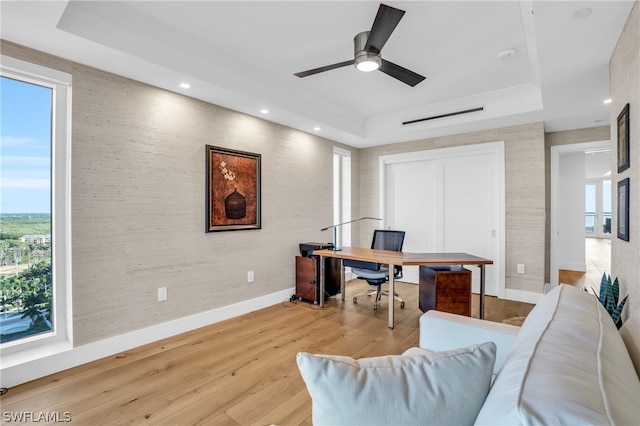 office featuring a tray ceiling, light hardwood / wood-style floors, and ceiling fan