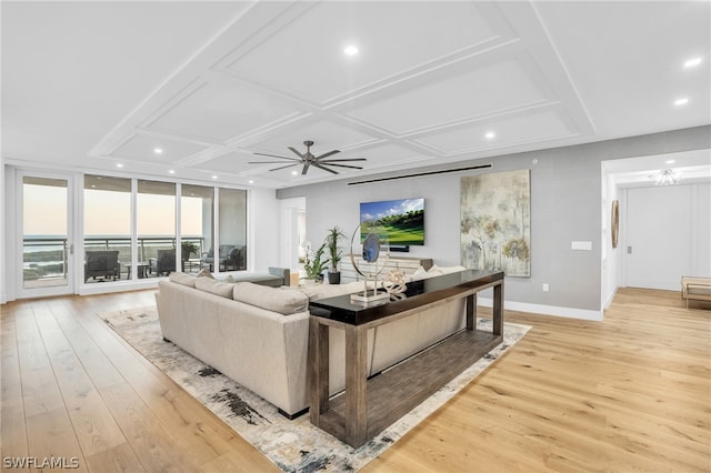 living room with coffered ceiling, ceiling fan with notable chandelier, light hardwood / wood-style floors, and a wall of windows