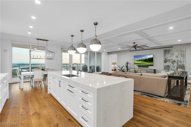 kitchen with white cabinets, a center island with sink, sink, and light hardwood / wood-style flooring