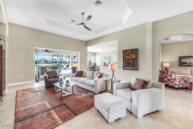 living area with a tray ceiling, light tile patterned flooring, arched walkways, visible vents, and a ceiling fan