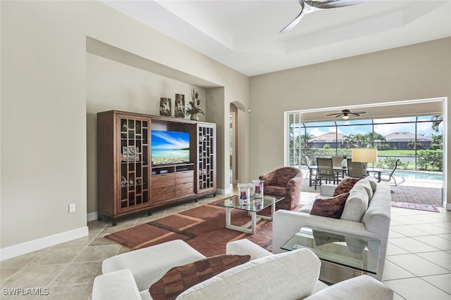 tiled living area featuring baseboards, ceiling fan, a towering ceiling, a raised ceiling, and arched walkways