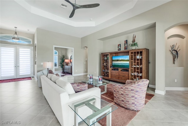 tiled living room with a tray ceiling, ceiling fan, and french doors