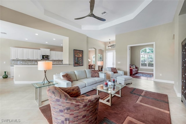 living room with ceiling fan, sink, a raised ceiling, and light tile patterned floors