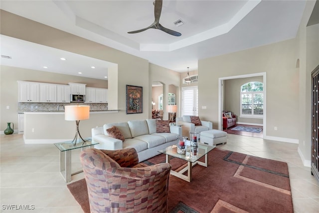 living room with visible vents, a ceiling fan, arched walkways, a tray ceiling, and light tile patterned floors