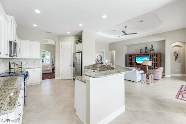 kitchen with appliances with stainless steel finishes, white cabinetry, an island with sink, light stone countertops, and ceiling fan