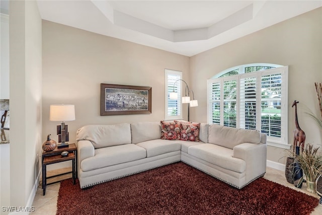 living area with light tile patterned flooring, a tray ceiling, and baseboards
