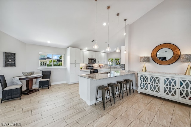 kitchen featuring light stone countertops, kitchen peninsula, tasteful backsplash, stainless steel appliances, and white cabinetry