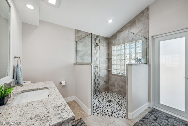 bathroom featuring a tile shower, tile flooring, vanity, and vaulted ceiling