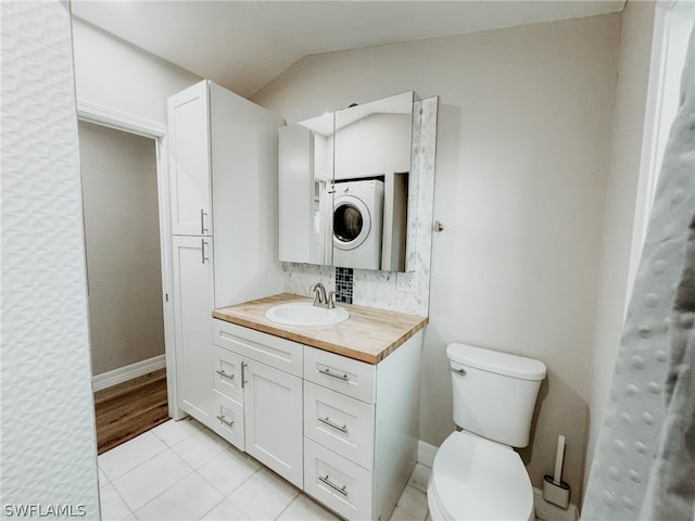 bathroom with stacked washer / dryer, tile flooring, lofted ceiling, vanity, and toilet