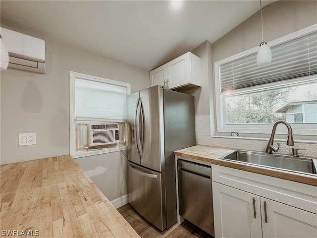 kitchen with hardwood / wood-style floors, stainless steel appliances, pendant lighting, wooden counters, and white cabinetry