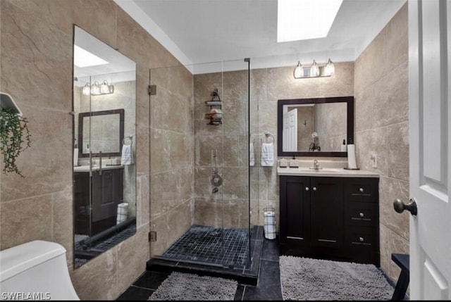 bathroom with tile flooring, a shower with shower door, tile walls, vanity, and toilet