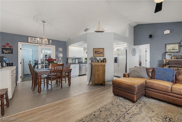 living room with ceiling fan with notable chandelier, light wood-type flooring, and lofted ceiling